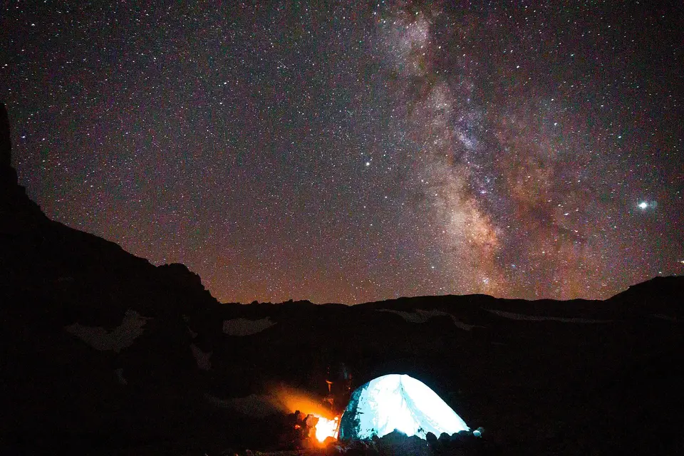 Aladağlar'da gece yıldızlı gökyüzünde Samanyolu, altta içi aydınlık çadır ve küçük kamp ateşi