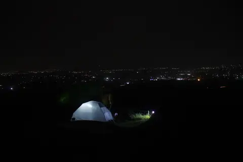 Gece tepede içeriden aydınlatılmış beyaz kubbe çadır, uzakta ovadaki yerleşim ışıkları
