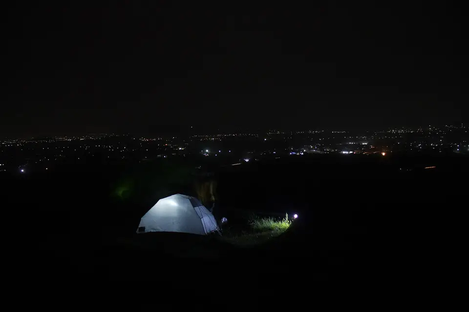 Gece tepede içeriden aydınlatılmış beyaz kubbe çadır, uzakta ovadaki yerleşim ışıkları
