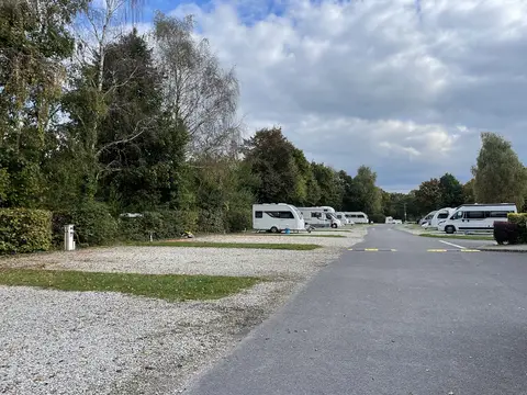 Ağaçlarla çevrili, çakıl zeminli düzenli karavan ve motokaravan kamp alanı