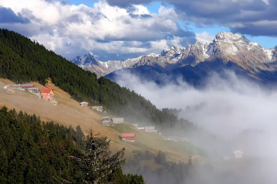 Sisli vadinin üzerinde yayla evleri, ormanlı yamaçlar ve karlı zirveler