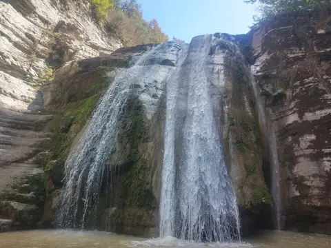 Kireçtaşı kaya duvarından iki kol hâlinde dökülen şelale